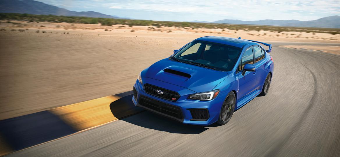 Blue Subaru WRX STI sports car driving on a desert race track, performance sedan